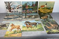 Ten vintage original paintings on board, arranged in two rows, showing various nature and rural themes including winter landscapes, horses, deer, and a lighthouse scene.