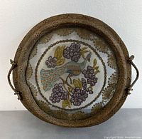 Front view of round wooden tray with embroidered peacock and flowers under glass or mesh cover
