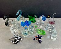 View of all 14 assorted glass mini figurines and paperweights showing animals and abstract shapes in multiple colors