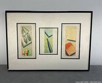 Framed artwork showing three vertical panels each with a still life composition including glasses, lipstick, pen, and books.
