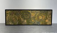 Full view of the framed mixed media art piece showing rectangular black frame and textured floral and circular elements.