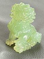 Front angle view of the translucent green jade Foo Dog figurine showing detailed carving of face and paws.