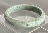 Close-up of green jade bangle on clear stand showing color and texture