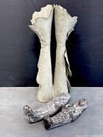 Photo showing two Egyptian-style clay ushabti figurines laid on their backs next to tall rolled slab ceramic vase with worn and chipped edges.