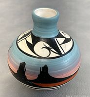 Front side of the signed Cedar Mesa vase showing the blue neck with black and white abstract patterns above a painted silhouette of mesas in dark silhouette against a reddish ground.