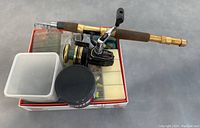 Fishing rod coiled with reel and multiple plastic storage containers on top of a box