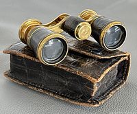 Close-up image of vintage French opera glasses resting on original black leather case showing wear and tear