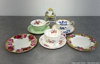 Front angle of the lot showing two dessert plates, three tea cups with matching saucers, and the Herend trinket box on gray surface.