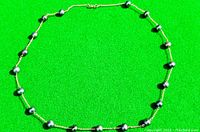 Full view of black pearl necklace laid on green background showing pearl spacing and chain style.