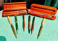 View of handcrafted pens made from wood and stone materials, along with two wooden pen cases containing four pens total.