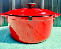Side view of red enamelled cast iron Dutch oven with lid and dual side handles, sitting on green surface.