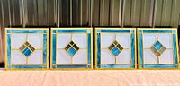 Four stained glass window panes set in yellow brass frames, arranged side by side showing front design.