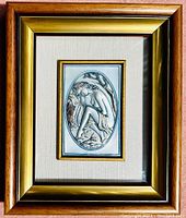 Full view of framed sterling silver .925 high relief wall art of a partially clad female figure seated by a tree and water with wood and golden frame.