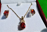 Close-up of garnet and white topaz necklace pendant and matching earrings in jewelry box under sunlight showing details of stones and setting.