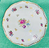 Top-down view of round porcelain platter displaying colorful floral patterns with gold accents on a white background.