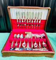 Full view of open wooden chest containing silver plated flatware organized in red felt compartments.