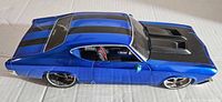 Side view of blue diecast car showing black racing stripes, raised hood vents, and chrome rims on tires