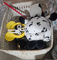 Basket containing a plush black and white spotted cow toy, a yellow plastic ring toy with rope handle, and other items.