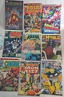 Top-down view of 9 vintage Marvel comic books including The Official Handbook of the Marvel Universe, Kid Colt Outlaw, Marvel Universe, Dazzler, Kazar the Savage, Morbius, Conan the Barbarian, Iron Fist, and a Dazzler variant.