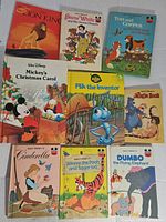 Top view of 10 vintage Disney children's books arranged in a group on a white surface featuring Lion King, Snow White, Tod and Copper, Mickey's Christmas Carol, Flik the Inventor, Jungle Book, Cinderella, Winnie the Pooh and Tigger Too, and Dumbo.