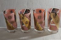 Photo showing four mid-century glasses with pink and gold geometric and emblematic designs, no visible chips or cracks.