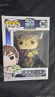 Front view of the Funko Pop box showing Luke Skywalker holding Yoda figure, single boxed collectible