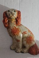 Photo showing full side profile of the Staffordshire pottery dog statue seated with orange-brown markings and gold collar.