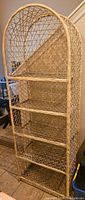 Full view of vintage metal frame wicker style bookshelf, showing arched top and four shelves.