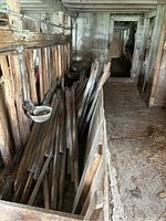 View down barn corridor showing multiple weathered wooden posts piled together with slanted ends visible