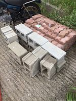Stack of gray concrete blocks and red interlocking paver stones on a concrete ground.