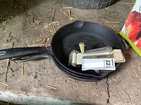 Three cast iron frying pans stacked with a vintage metal can opener resting inside the smallest pan. The pans show signs of use and some dirt.