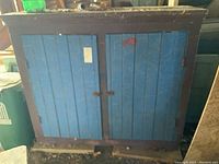 Front view of wooden cupboard, showing blue paneled doors with dark brown frame and metal latch
