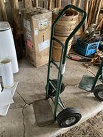 Front angle view of the metal dolly showing the green frame, handle, pneumatic tires, and base plate.