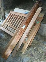 Wooden bed frame components stacked showing headboard with vertical slats and side rails with natural wood grain finish.