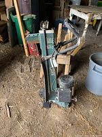 Full vertical photo of the Yardworks electric log splitter standing on dirt floor in barn environment, showing motor, control handle, and splitting wedge.