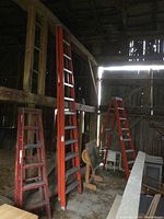 Overall view of orange fibreglass ladder leaning in barn among other ladders
