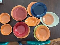 Top down photo of 10 Fiestaware dishes arranged on a table. Bowls and plates in various colors including orange, red, blue, yellow, and cream.