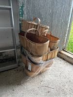 Stack of six vintage wooden fruit baskets with handles, some wrapped in plastic, stored in a barn corner.