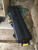 Full view of closed black plastic heavy duty hunting case on ground showing elongated shape and ribbed lid.