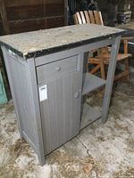 Front view of the gray painted wooden storage cabinet showing the drawer, door, and black top surface with wear.