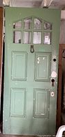 Full view of green painted wood door with rectangular panels and nine glass window panes at top.