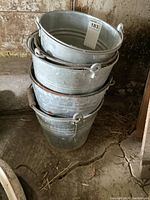 Stack of five vintage metal pails with attached handles and signs of rust and dents.