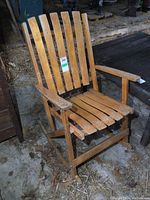Front angle view of a solid wood folding rocking chair showing vertical slat back and seat, curved armrests, and worn finish.