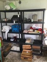 Two black resin shelving units with multiple shelves, some contents on the shelves but not included in the sale.