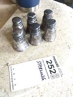 Six sterling silver shakers arranged in two rows with visible tarnish and patina.