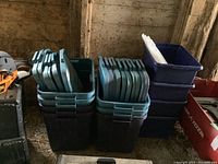 Photo of multiple dark green/black plastic tote bins stacked, with lids placed on top of each bin.
