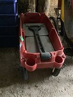 Red plastic wagon viewed from front with handle inside the bed, two integrated cup holders in front corners, black wheels with white hubs visible.