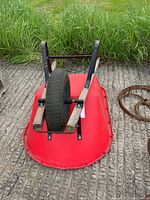 View of the red plastic wheelbarrow flipped upside down showing the single pneumatic tire mounted on black metal frame with wooden handles.