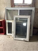 Four vinyl framed windows stacked on floor, in a rustic space.