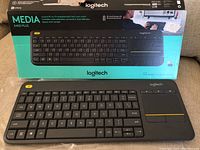 Logitech Media K400 Plus keyboard in front of the original packaging box featuring product image and branding.